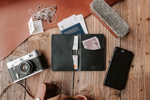 Flat lay of traveler essentials including wallet, camera, and phone on wooden surface.
